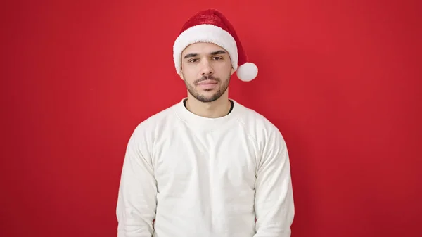 Junger Hispanischer Mann Lächelt Selbstbewusst Mit Weihnachtsmütze Über Isoliertem Rotem — Stockfoto