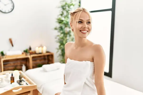 Young caucasian woman wearing towel sitting on massage board at beauty salon