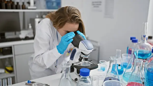 迷人的金发女科学家专心致志地投入到医学研究中 她在实验室里用显微镜描绘出了一个致力于科学分析的决心的肖像 — 图库照片