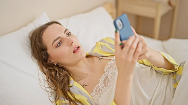 年轻的金发女人用智能手机躺在床上 — 图库照片