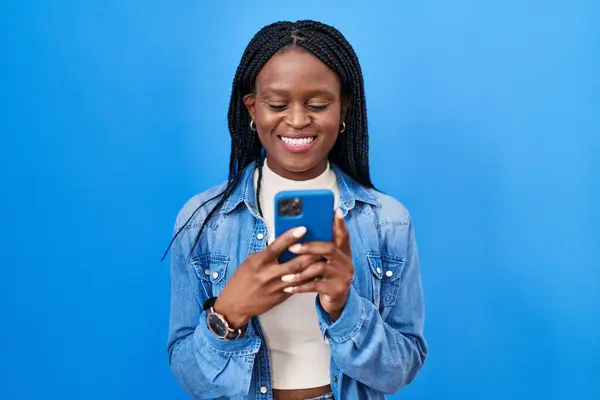 stock image African woman with braids using smartphone typing message looking positive and happy standing and smiling with a confident smile showing teeth 