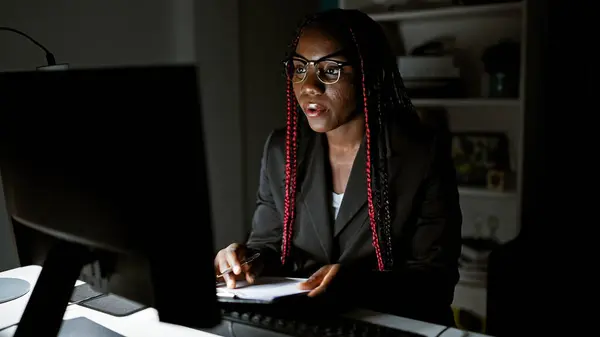 Working night magic, african american business woman rocks it at the office, taking notes and juggling a video call. portraying success she commands the interior room with confidence