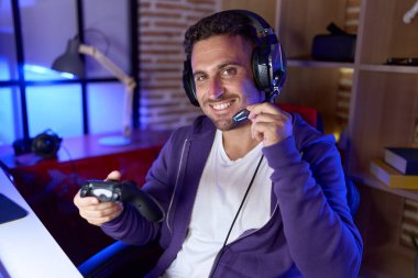 Young hispanic man streamer playing video game using joystick at gaming room