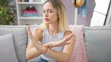 Kanepede oturan genç sarışın kadın ciddi bir yüzle el ele tutuşuyor.