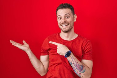 Kırmızı arka planda duran İspanyol genç adam kameraya hayret ediyor ve gülümsüyor.. 