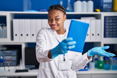 Örgü ören Afrikalı Amerikalı bir kadın bilim adamı laboratuvarında çalışıyor. Mutluluk dolu bir gülümsemeyle başarıyı kutlayan tabletle video çağrısı yapıyor. 