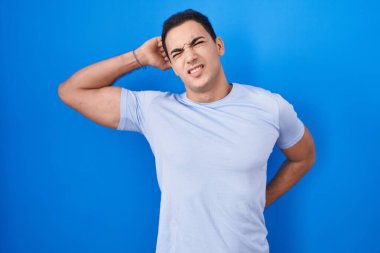 Young hispanic man standing over blue background stretching back, tired and relaxed, sleepy and yawning for early morning 