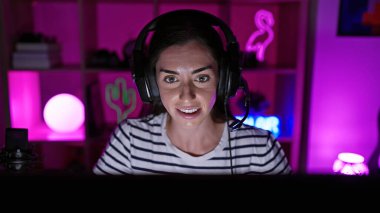 Çekici, genç İspanyol kadın, gülümseyen ve kendinden emin, oyun macerasını yaşıyor, karanlık bir gecede oyun odasında kulaklık takıyor, sanal bir dünyada büyüleniyor.