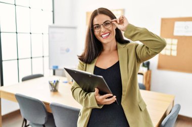 Genç, güzel, İspanyol bir iş kadını. Ofiste elinde bir panoyla gülümsüyor.