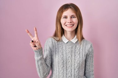 Pembe arka planda duran güzel bir kadın iki numarayı gösterip işaret ederken kendinden emin ve mutlu bir şekilde gülümsüyor.. 