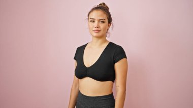 İzole edilmiş pembe arka planda gevşek bir ifadeyle spor kıyafeti giyen genç ve güzel bir İspanyol kadın.