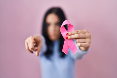 Elinde pembe kanser kurdelesi olan İspanyol bir kadın kamerayı işaret ediyor ve sen kendine güvenen ciddi bir hareket yapıyorsun. 