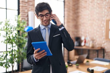 Genç İspanyol iş adamı. Ofiste dokunmatik ped kullanarak akıllı telefondan konuşuyor.