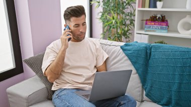 Ciddi telefon konuşmalarına dalmış, evdeki oturma odasındaki kanepede rahatça otururken dizüstü bilgisayar kullanan Latin kökenli genç bir adam.