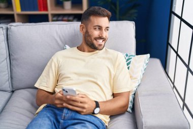 Evdeki kanepede oturan, akıllı telefon kullanan genç bir İspanyol.