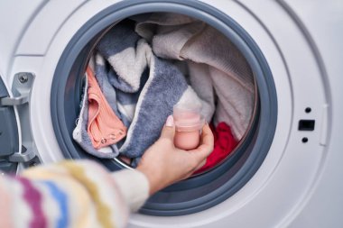 Young caucasian woman pouring detergent on washing machine at laundry room