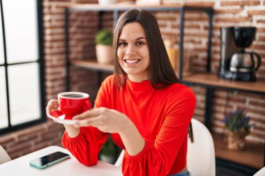 Young beautiful hispanic woman drinking coffee sitting on table at home
