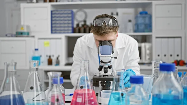 stock image Handsome young caucasian man, a dedicated scientist, deeply engrossed in analyzing samples under the microscope at a professional medical lab.