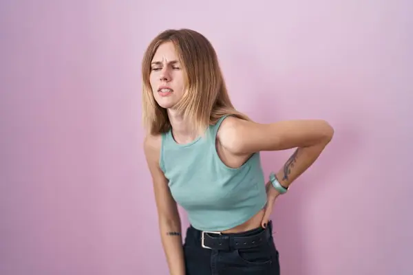金发女人站在粉红的背脊上 用手触摸 肌肉疼痛 — 图库照片