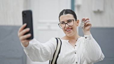 Genç ve güzel bir İspanyol kadın yeni evin ön kapısında anahtarlarını gösterirken fotoğraf çekiyor.