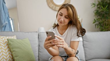 Genç kadın evde koltukta oturan smartphone kullanarak