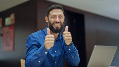 Genç İspanyol iş adamı bilgisayarı kullanarak ofiste baş parmak hareketi yapıyor.