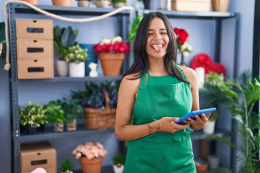 Çiçekçi dükkanında çalışan esmer bir kadın elinde tabletle mutlu bir ifadeyle dilini dışarı çıkarıyor.. 