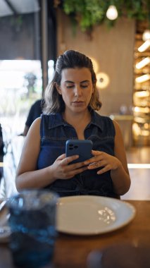Genç ve güzel İspanyol kadın restoranda masanın üzerinde akıllı telefon kullanıyor.