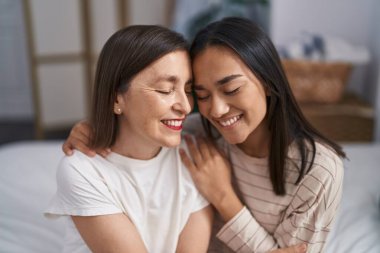 Two women mother and daughter hugging each other sitting on bed at bedroom