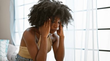 Afro-Amerikalı kadın evde kanepede oturup baş ağrısı çekiyor.