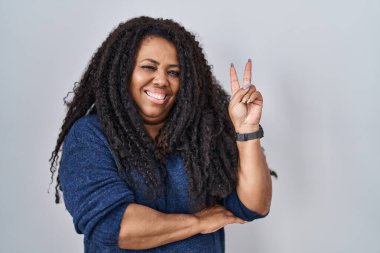 Ayrıca beyaz arka planda durup gülümseyen, kameraya göz kırpan, zafer işareti yapan İspanyol bir kadın. İki numara.. 