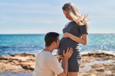 Erkek ve kadın çift sahilde göbeğini öpüyorlar.