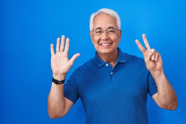 Mavi arka planda gri saçlı, orta yaşlı bir adam 7 numaralı parmaklarıyla işaret ederken kendinden emin ve mutlu gülümsüyor.. 