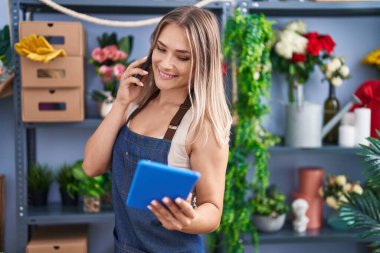 Young caucasian woman florist talking on smartphone using touchpad at florist