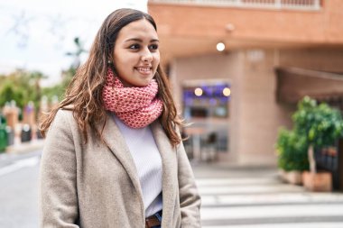 Young beautiful hispanic woman wearing scarf looking to the side at street