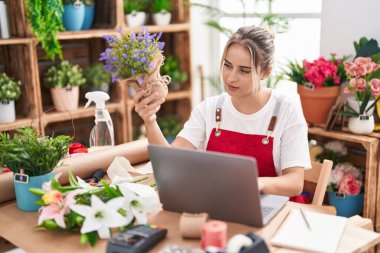 Young blonde woman florist using laptop holding lavender plant at flower shop
