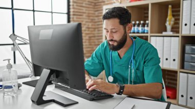 Genç İspanyol doktor klinikte bilgisayar kullanıyor.