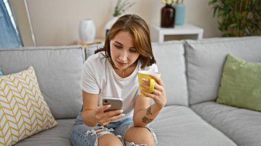 Young woman using smartphone drinking coffee at home
