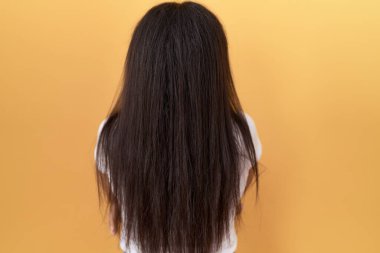 Sarı arka plan üzerine günlük beyaz t-shirt giyen genç Arap kadın arkasını dönüp kollarını kavuşturarak diğer tarafa bakıyor. 