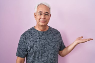 Pembe arka planda gri saçlı orta yaşlı bir adam. Gülümsüyor, avucunun içi gibi kameraya bakıyor.. 