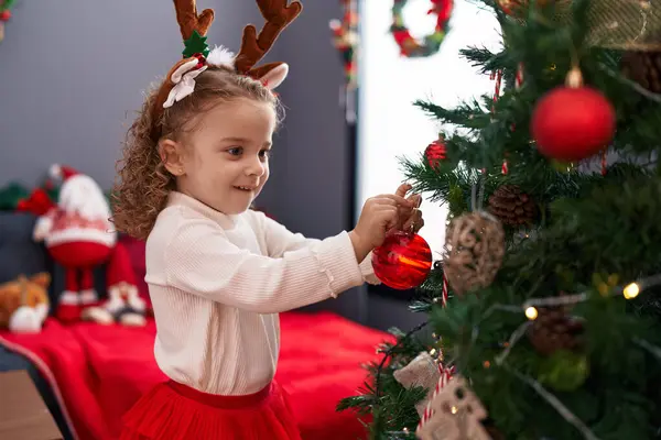 自宅でクリスマスツリーを飾るトナカイ耳を着用する愛らしいブロンドの少女 — ストック写真