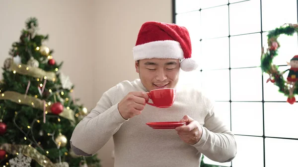 自宅でクリスマスツリーで立っているコーヒーを飲む若い中国人男性 — ストック写真