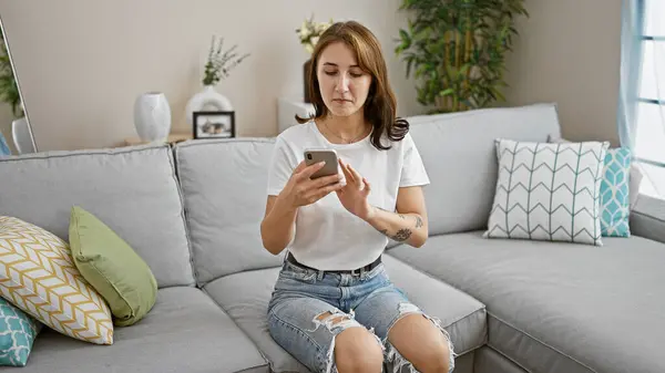 在家中使用智能手机的年轻女子坐在沙发上 — 图库照片
