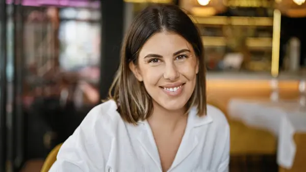 Young beautiful hispanic woman smiling happy sitting on the table at the restaurant