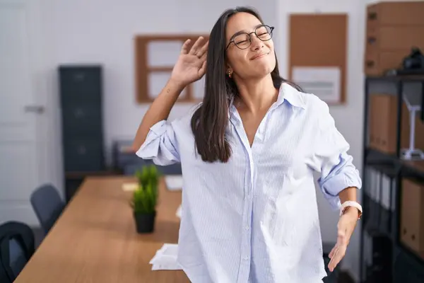 Young hispanic woman at the office stretching back, tired and relaxed, sleepy and yawning for early morning