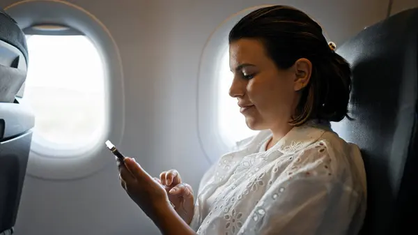 在飞机上使用智能手机的年轻美丽的惊慌失措的女人 — 图库照片