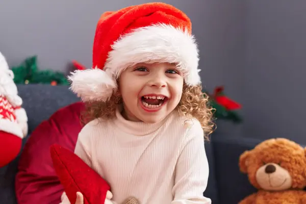 家のクリスマスの装飾によってソファーに座ってサンタクロースの人形を抱擁する愛らしいブロンドの少女 — ストック写真