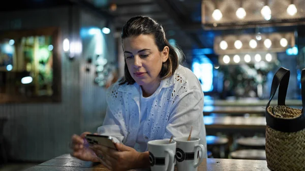 Beautiful young hispanic woman using smartphone at cafeteria