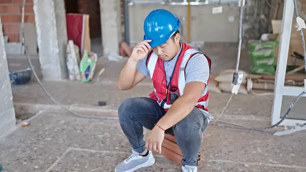 builder tired sitting on floor with serious expression at construction site