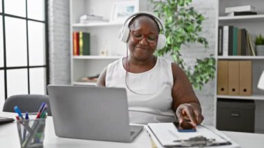 Gülümseyen Afro-Amerikan kadın, örgülü patron, dans ederken başarıdan zevk alan, iş yerinde telefonla müzik dinleyen.